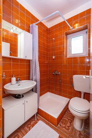 A bathroom with orange tiles, a white sink, a shower, and a toilet. - Room-cozy Room Near Beach D (Novalja)