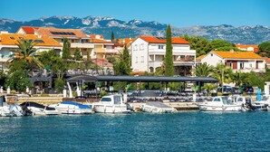 A marina with boats docked, a covered seating area, and buildings with red-tiled roofs. - Room-cozy Room Near Beach D (Novalja)