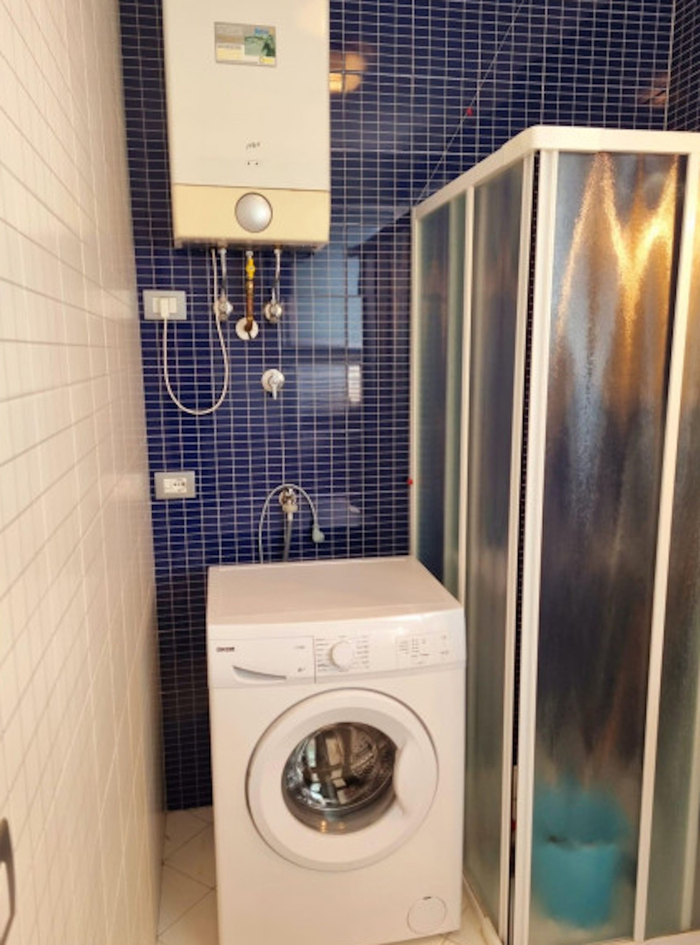 A compact bathroom with a built-in washing machine, a shower enclosure, and a wall-mounted heater.
