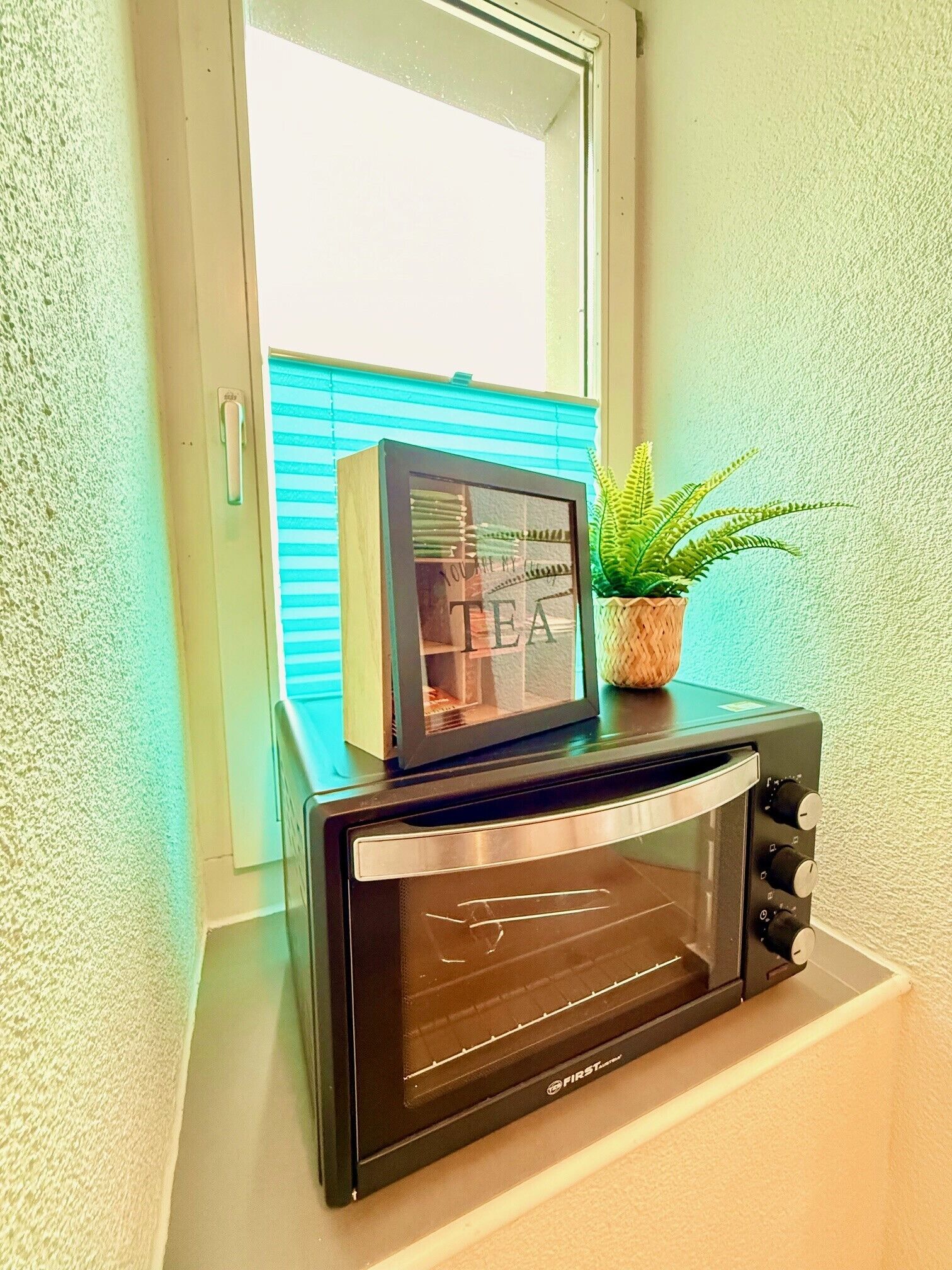 Ein schwarzes Toaster-Heizgerät mit Glastür, platziert auf einer Arbeitsplatte neben einem Fenster mit Jalousien.