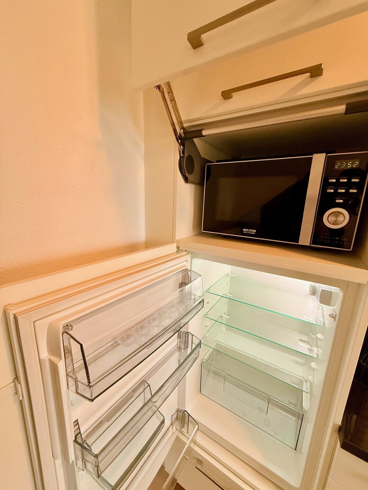 Uma cozinha compacta com micro-ondas acima de uma geladeira, ambos com portas de vidro transparente.