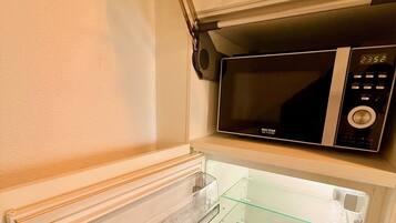 Uma cozinha compacta com micro-ondas acima de uma geladeira, ambos com portas de vidro transparente.