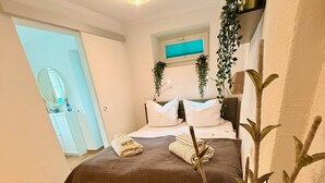 A bedroom with a bed, bedside tables, a mirror, and a potted plant.