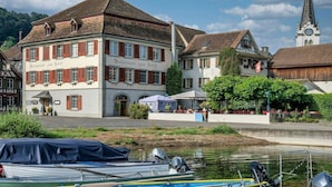 A traditional building with a sign reading "Restaurant zum Schopf" and a church with a steeple in the background.