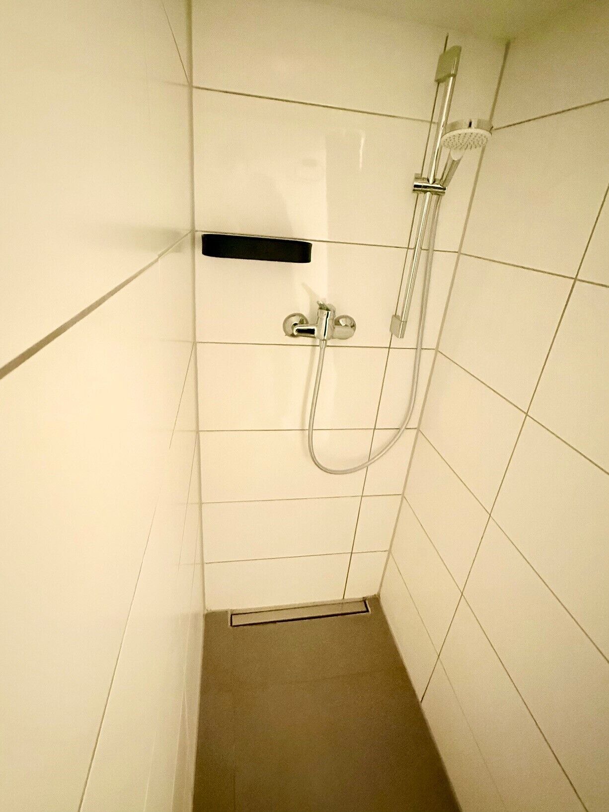 Une petite cabine de douche carrelée, équipée d’un pommeau de douche à main et d’un robinet mural.