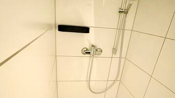 A small, tiled shower stall with a handheld showerhead and a wall-mounted faucet.