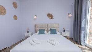 A neatly made bed with two pillows, a bedside table with a lamp, and decorative wall art. - GIN Wellness Hotel (Santorini)