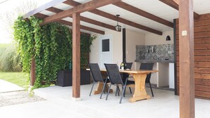 An outdoor patio with a wooden pergola, a dining table with chairs, and a kitchen area with a tiled backsplash. - Villa Casa Kalandra ZadarVillas (Rovinj)