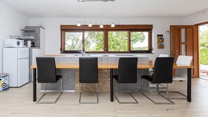 A modern kitchen with a central island, black chairs, a white refrigerator, and a window with a view of trees. - Villa Casa Kalandra ZadarVillas (Rovinj)