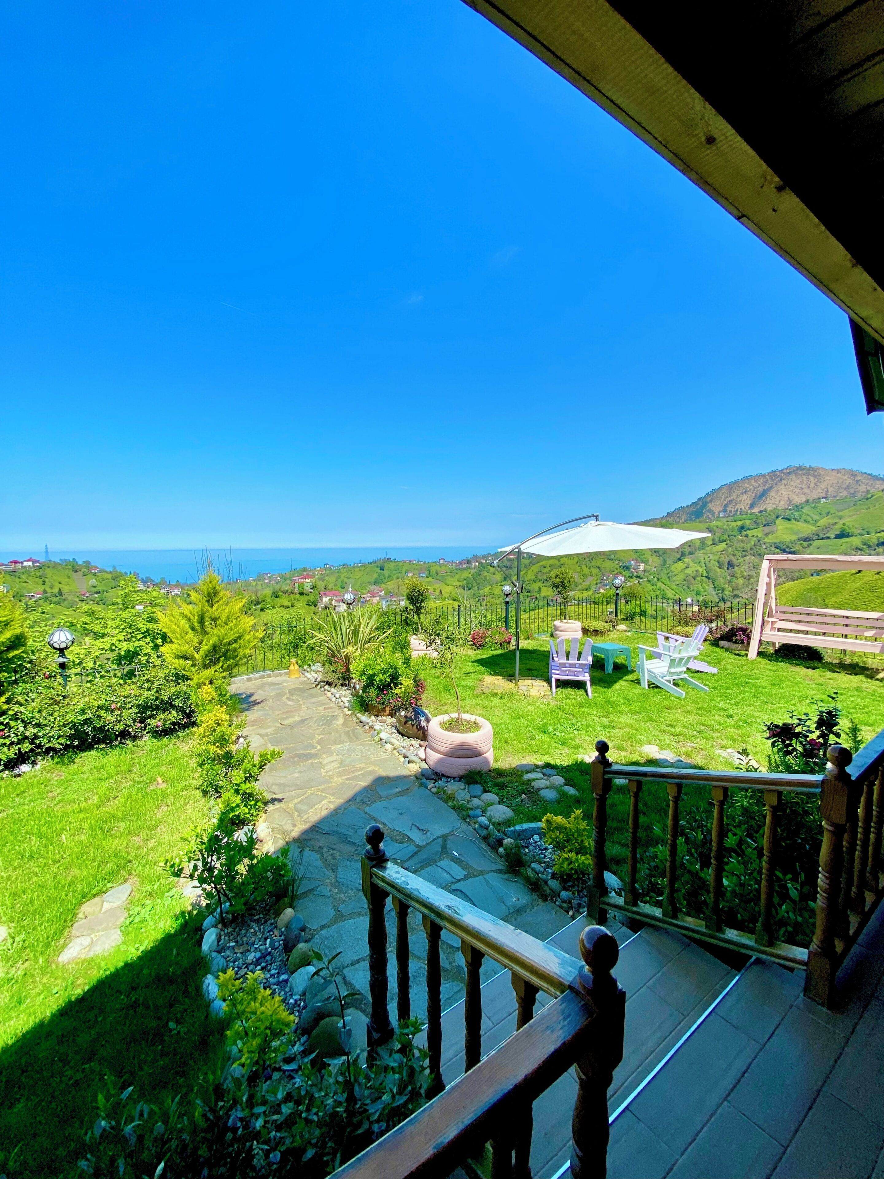 Un jardin avec un chemin de pierres, du mobilier d’extérieur et une vue sur la mer et les collines.