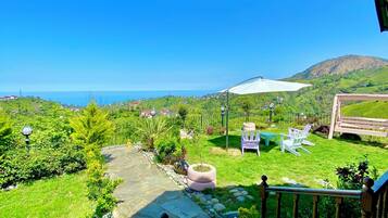 Un jardin avec un chemin de pierres, du mobilier d’extérieur et une vue sur la mer et les collines.