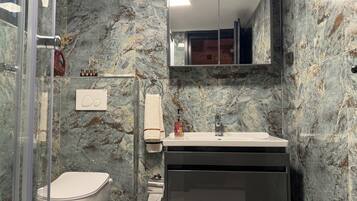 A bathroom with a marble wall, a toilet, a sink with a mirror above it, and a towel rack.