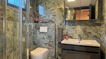 Un baño con cabina de ducha de vidrio, inodoro, lavabo con espejo y paredes de mármol.