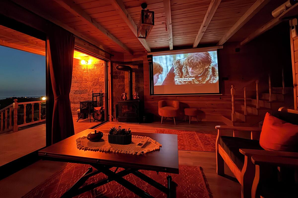 Una habitación acogedora con chimenea, pantalla de proyector y una mesa con tetera y plantas.