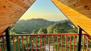 A wooden balcony with a view of a hilly landscape.