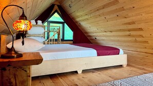 Een knus slaapkamer van een houten chalet met een bed, een hanglamp en uitzicht op de natuur.