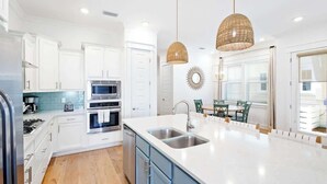 A modern kitchen with white cabinets, stainless steel appliances, a large island with a sink, and wicker pendant lights.