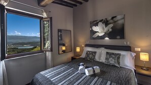 Um quarto com uma janela grande, uma cama com almofadas, um abajur e um quadro de uma flor.