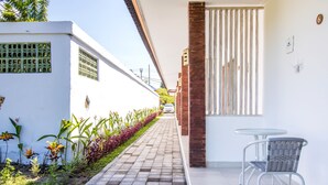 A narrow pathway leading to a white building with a glass door and a small table with a chair. - OYO 2896 Uma Menuh Guest House Near Pantai Keramas (Perean Tengah)