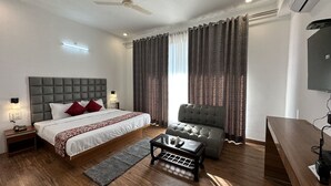 Une chambre d’hôtel moderne avec un grand lit, un canapé gris, une petite table et un ventilateur de plafond.