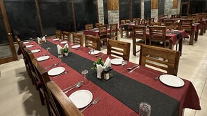 Un espace repas avec des tables dressées pour plusieurs personnes, des chaises en bois et une nappe rouge.