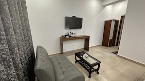 Un salon moderne avec un canapé gris, une table basse, un téléviseur posé sur un meuble en bois et une porte visible au fond.