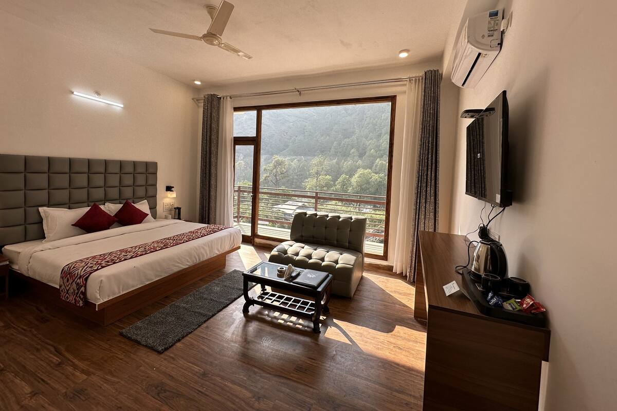 A modern hotel room with a large bed, a sofa, a coffee table, and a TV.