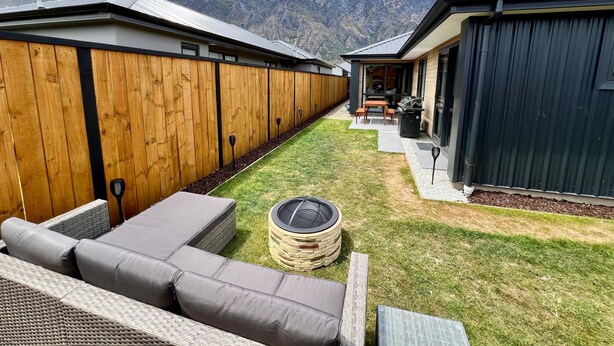 Eine moderne Terrassengrundstück mit Holzzaun, einer Sitzgruppe mit Kissen, einem Grill und Blick auf Berge.