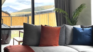 Ein modernes Wohnzimmer mit großem Fenster, Blick auf Berge und einem Holzzaun davor.