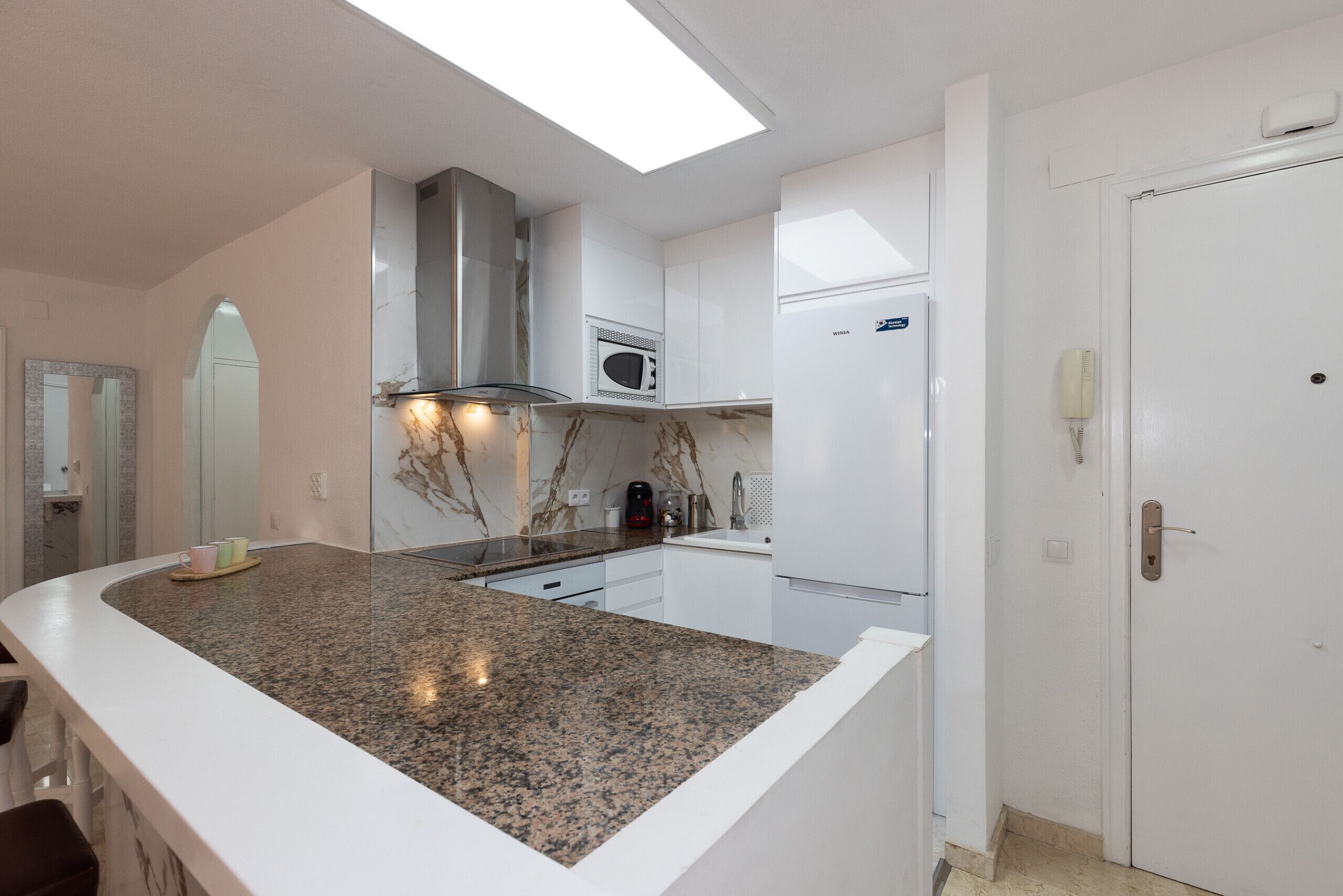 Eine moderne Küche mit einer Granitarbeitsplatte, weißen Schränken, einer Mikrowelle und einem eingebauten Backofen.