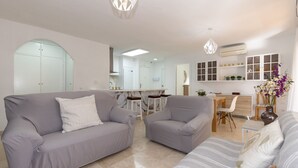 Ein modernes Wohnzimmer mit grauen Sofas, einem gestreiften Sofa und einem Essbereich mit Tisch und Stühlen.