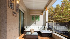 Ein sonniger Balkon mit einer weißen Couch, Korbmöbeln und hängenden Pflanzen.