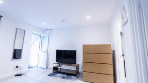 A modern living room with a flat-screen TV on a wooden stand, a large wardrobe, and a door leading to another room. - Cosy Hideaway Close to Town (Reading)