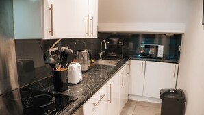 A modern kitchen with white cabinets, a black countertop, a stainless steel stove, a coffee maker, and a trash bin. - Cosy Hideaway Close to Town (Reading)