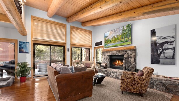 A spacious living room with a stone fireplace, wooden ceiling beams, and large windows with blinds. - Ridge Court # 14 at Palisades - Ski Shuttle, Dog OK (Olympic Valley)