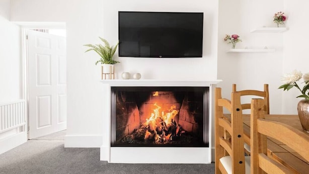 A living room with a fireplace, a flat-screen TV mounted above it, and a dining area with wooden chairs and a table.