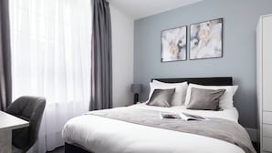 A modern hotel room with a large bed, a desk, and a chair. There are two abstract paintings on the wall.