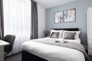 A modern hotel room with a large bed, a desk, and a chair. There are two abstract paintings on the wall. - Beautiful Central 4 Bedroom Apart next2 KingsCross (Greater London)