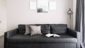 A black leather sofa with two cushions, a floor lamp, and three framed pictures on the wall.