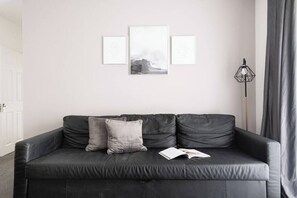 A black leather sofa with two cushions, a floor lamp, and three framed pictures on the wall. - Beautiful Central 4 Bedroom Apart next2 KingsCross (Greater London)