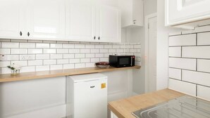 A kitchen with white cabinets, a microwave, a small refrigerator, and a wooden countertop.