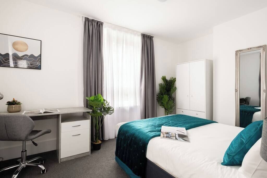 Ein Hotelzimmer mit Bett, Schreibtisch, Stuhl, Kleiderschrank und einem großen Fenster mit Vorhängen.