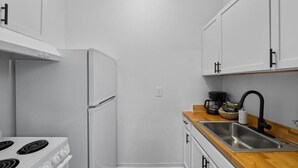 A compact kitchen with white cabinets, a stainless steel sink, and a stove. - Cozy 1BR Near Zoo, UC, Hospitals (Cincinnati)