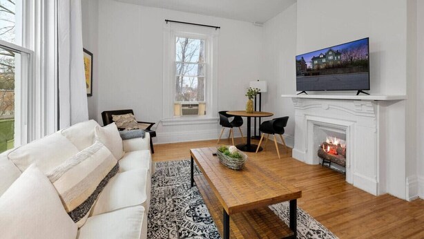 A living room with a white sofa, a wooden coffee table, a fireplace, and a television on a mantel. - Cozy 1BR Near Zoo, UC, Hospitals (Cincinnati)
