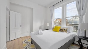 A hotel room with a bed, a window with curtains, a bedside table, and a view of buildings outside. - Cozy 1BR Near Zoo, UC, Hospitals (Cincinnati)