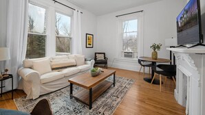 A spacious living room with a white sofa, a wooden coffee table, and a fireplace. - Cozy 1BR Near Zoo, UC, Hospitals (Cincinnati)