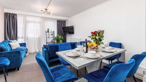 A modern dining area with a grey table set for four, blue upholstered chairs, and a flat-screen TV mounted on the wall. - Modern 4 Bed Apartment  next to Borough Station (Greater London)