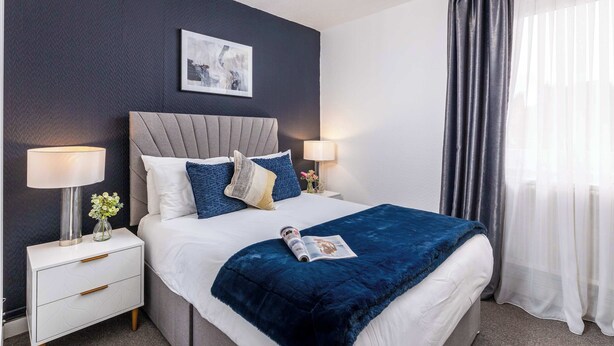 A neatly made bed with a dark blue blanket, two bedside lamps, and a framed picture on the wall. - Modern 4 Bed Apartment  next to Borough Station (Greater London)