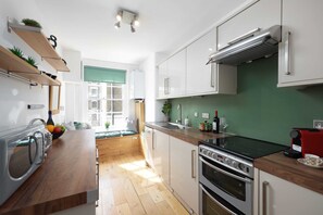 Una cucina moderna con forno integrato, macchina del caffè e lavello. Sono presenti mensole in legno con piante e una finestra vista esterna.