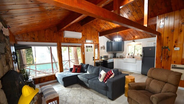 A cozy cabin interior with a wooden ceiling, a sofa, a recliner, a dining area, and a stone fireplace. - Bear Paw- Lake Area  located in Willow Cove (Bass Lake)